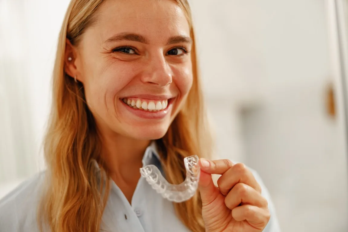 Young woman holding a clear aligner tray and comparing treatment options at Peninsula Dentistry in Huntington Beach